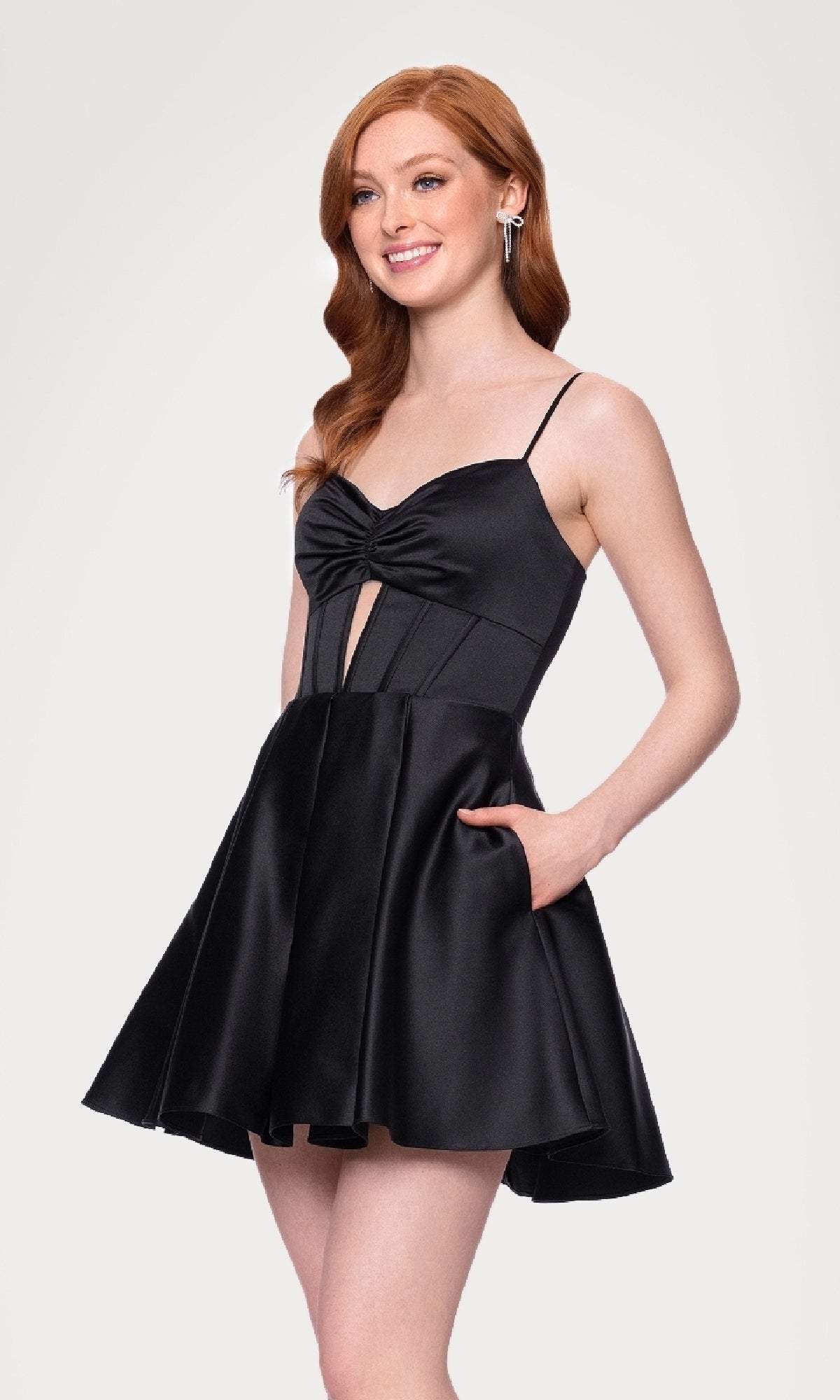 Model wears the Cut-Out Black Mini Hoco Dress: Blondie Nites 5605BN, a sleeveless short black dress with a fitted bodice, front cut-out, and flared skirt, standing against a plain light background.